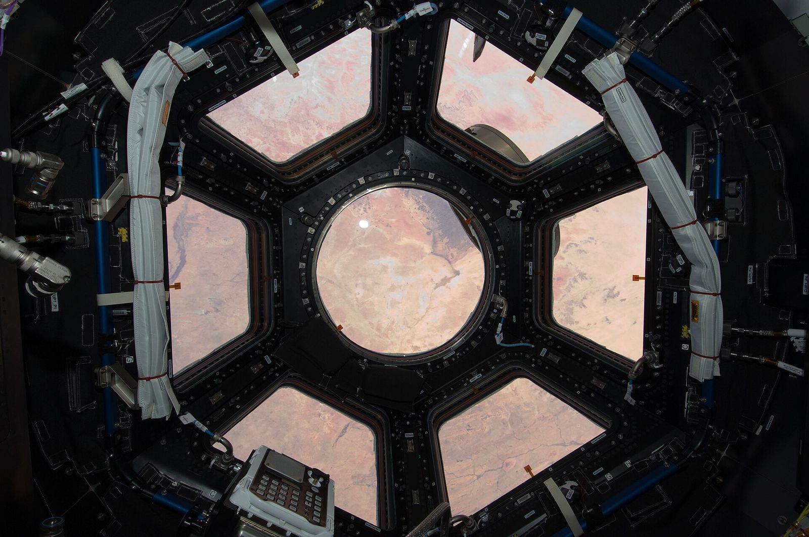 The seven-window cupola of the International Space Station with its shutters open, the Earth beyond.